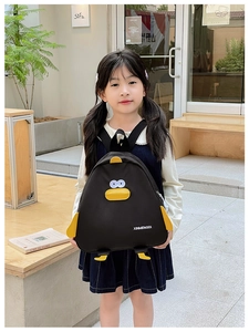 Détail d'un sac à dos canard 3D jaune tenu par une petite fille dans un café en plein air
