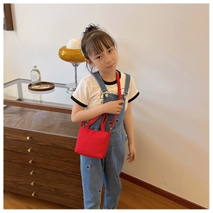 Close-up of a child wearing a stylish red canvas shoulder bag with denim overalls