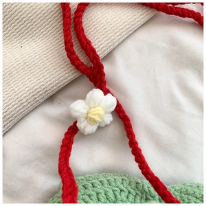 Close-up of handmade crochet strawberry bag showing green knit texture and white flower detail