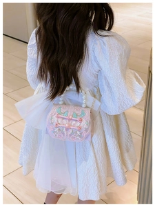 Detail of pink embroidered kids purse with pearl handle and silk bow on white dress