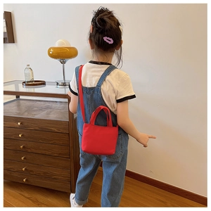 Child wearing a bright red mini canvas crossbody bag in a stylish home setting