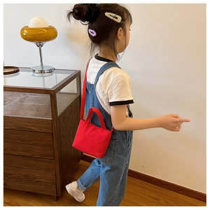 Children's red canvas crossbody bag shown by a model in a warm home interior setting