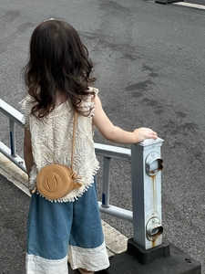Detailed view of child wearing a round brown crossbody bag with a smile face emoji