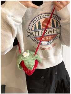 Detail of a handmade strawberry crochet crossbody bag with white flower and red knit strap