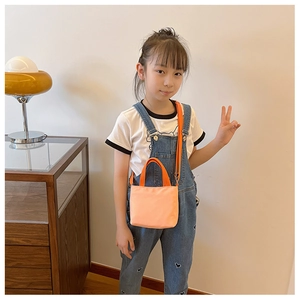 Girl wearing a bright orange crossbody bag with casual denim overalls in a home setting