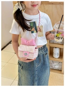 Close-up of pink tweed girl's crossbody bag with bow detail and chain strap worn by model