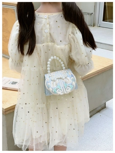 Detailed close-up of blue silk embroidery bag with pearl handle on child model