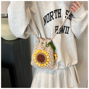 Detail of handmade crochet sunflower bag with woven strap and green leaf tassel accents