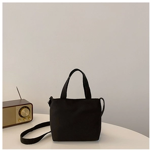 Close-up of minimalist black canvas mini tote bag with adjustable shoulder strap and dual handles