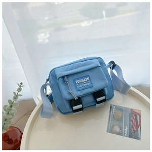Gros plan du sac bandoulière enfant en toile bleu clair avec boucles et logo brodé