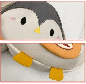 Detail of penguin crossbody bag showing 3D embroidery and contrasting gray-white-yellow fabric