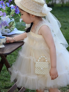 Close-up of girl's cream mesh princess dress with pearl straps and woven handbag