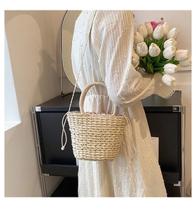 Detail of hand-woven straw bucket bag featuring a drawstring closure and a sturdy handle