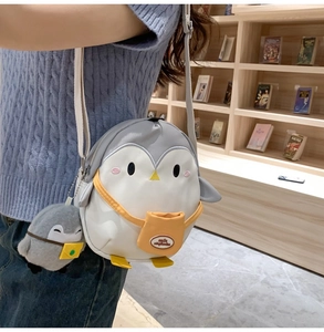 Detail of penguin crossbody bag with plush charm and adjustable shoulder strap on a child