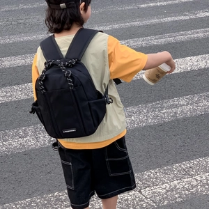 Außenansicht eines Kindes mit schwarzem Nylon-Rucksack mit Modelabel und Kordelzug-Detail