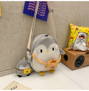 Detail of penguin crossbody bag with a plush penguin keychain and adjustable strap