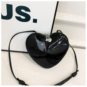 Détail d'un sac bandoulière noir en forme de cœur en cuir verni brillant avec zip argenté