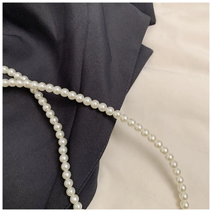 Close-up of white round pearls with glossy finish on a diagonal crossbody bag strap