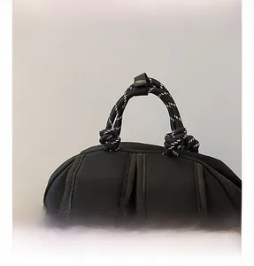 Detail eines schwarzen Segeltuch-Rucksacks mit schwarz-weiß gewebtem Seilgriff und Metallschnalle