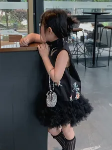 Detail of child wearing black embroidered qipao dress with a silver rhinestone handbag
