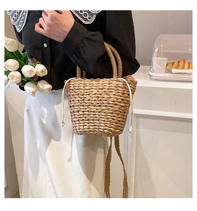 Detailed view of handmade woven straw bucket bag with white drawstring closure and top handles