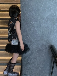 Detail of child wearing a black qipao tulle dress with silver rhinestone chain bag