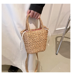 Detail of hand-woven straw bucket bag featuring a red and white checkered drawstring liner