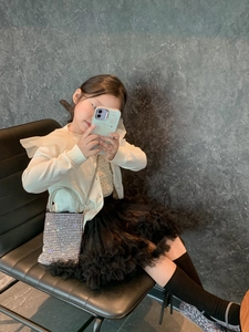 Detail of silver rhinestone crossbody bag paired with a white ruffled cardigan and tutu