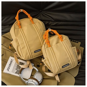 Detail der khakifarbenen Kordelzug-Rucksäcke mit orangen Seilgriffen und Fashion-Labels