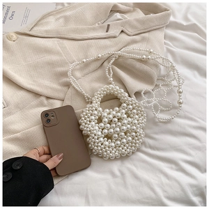 Macro detail of a mini white handmade pearl woven handbag with a long pearl strap