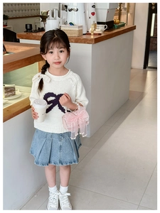 Detail of girl's knit sweater with purple bow and a pearl handle handbag in a cafe setting