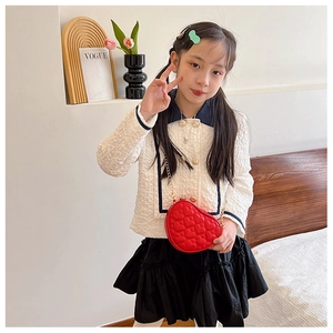 Close-up of red heart-shaped quilted bag with gold chain strap on a child model