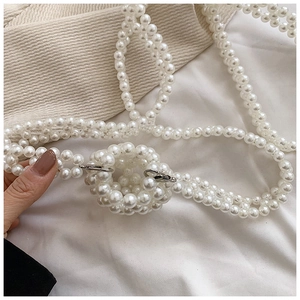 Détail d'une chaîne en perles blanches avec breloque ronde et fermoir argenté sur le sac