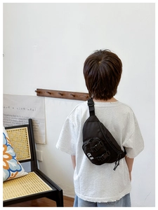 Rear view of child wearing black nylon chest bag with adjustable strap and white text logo