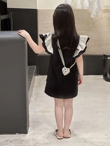 Détail d'une robe noire pour fille avec volants blancs et un sac à bandoulière en perles