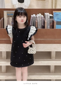 Detail of girls' black dress with white ruffle sleeves and a pearl woven handbag