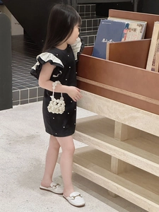 Detail of girl's black dress featuring white ruffled sleeves and a mini pearl handbag