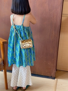 Detail of a kids' gold quilted chain bag paired with a green floral dress