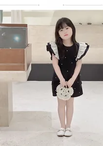 Close-up of elegant black kids dress featuring 3D white ruffles and pearl decorations