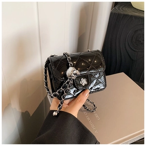 Detail of glossy black patent leather mini bag with diamond quilting and flower clasp