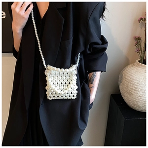 Détail d'un mini sac en perles blanches avec chaîne bandoulière sur blazer noir