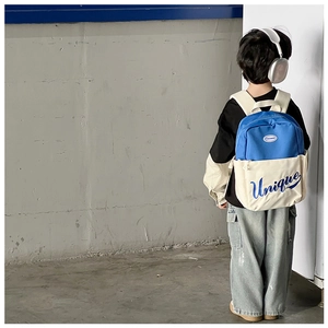 Rear view of a child wearing the blue and beige color-block backpack against a gray wall