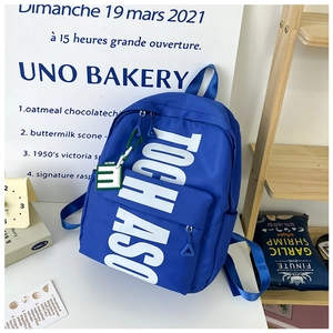 Detail of royal blue school backpack with white TOCH ASO letter print and creative charm