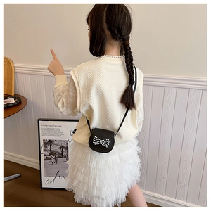Détail d'un mini sac bandoulière noir avec un nœud en perles blanches pour tenues d'enfants