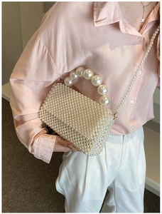 Detailed view of woven pearl handbag featuring beaded top handle and crossbody strap