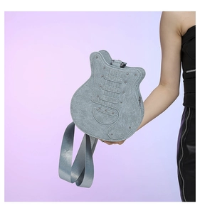 Detail of light blue guitar shaped shoulder bag featuring metal studs and wide fabric strap