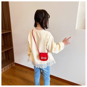 Détail du mini sac bandoulière rouge avec nœud en perles sur pull crème et jean