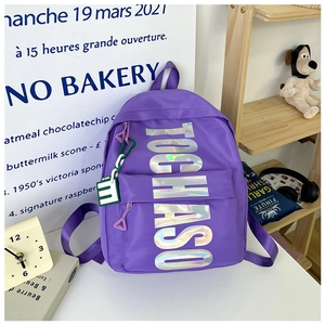 Detail of purple nylon school bag with silver laser lettering and green accessory charm