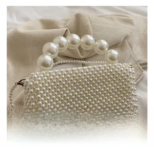Detailed view of the elegant pearl beaded handle and woven white texture of the square bag