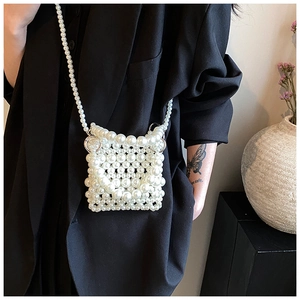 Détail d'un mini sac bandoulière en perles blanches porté sur une veste noire
